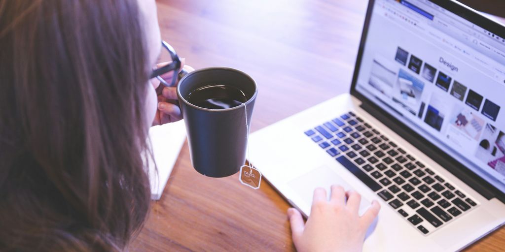 woman holding tea filled mug using MacBook